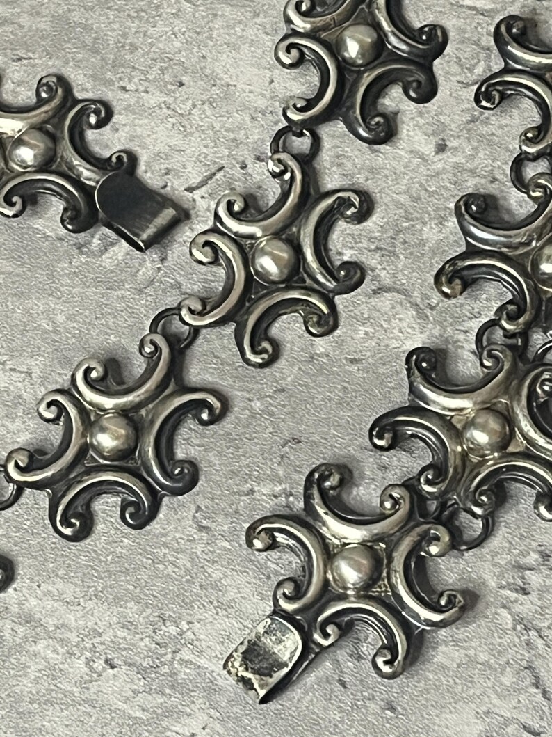 Peut inclure: Un collier en argent avec un design orn&eacute; et d&eacute;taill&eacute;. Chaque maillon pr&eacute;sente une forme circulaire stylis&eacute;e avec une perle centrale en relief. La cha&icirc;ne est compos&eacute;e de maillons entrelac&eacute;s, cr&eacute;ant un motif continu.