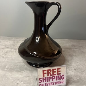 May include: A black ceramic vase with a wide mouth and a handle. The vase has a glossy finish and a unique, curved design.