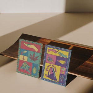 May include: Two colorful art prints with cannabis-themed illustrations. One print features a marijuana leaf, a lighter, and other related images. The second print has the text "In weed we trust" and other cannabis-related graphics.