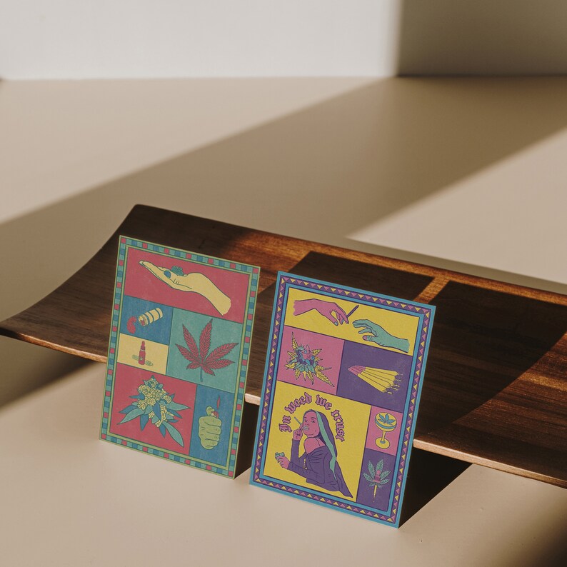May include: Two colorful art prints with cannabis-themed illustrations. One print features a marijuana leaf, a lighter, and other related images. The second print has the text "In weed we trust" and other cannabis-related graphics.