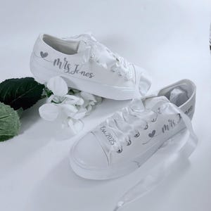 Flat Slip On Bride, two white canvas sneakers with satin laces. One shoe has the text 'Mrs. last name marriage' and a small heart design. The other shoe has the text 'Est. time' and a small heart design.