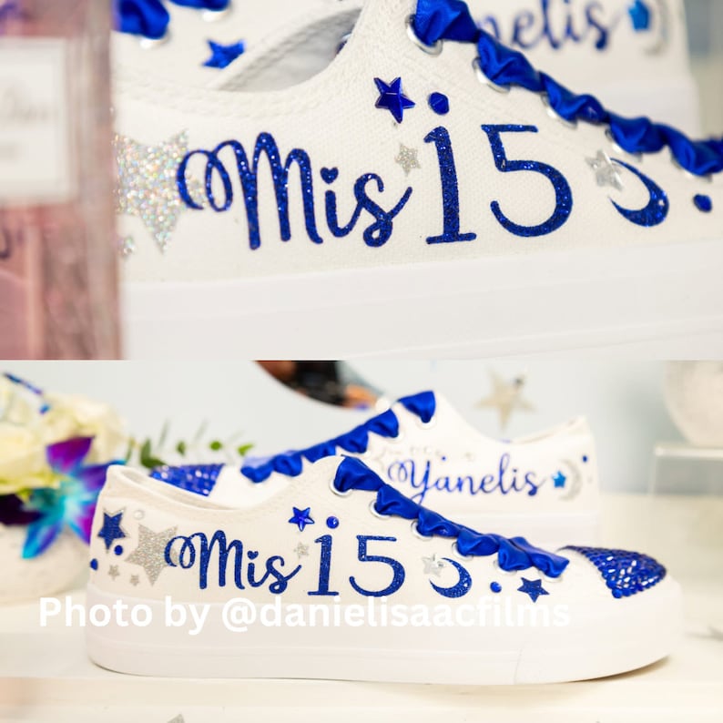 Puede incluir: Zapatillas blancas de lona con detalles de cinta azul y estrellas plateadas brillantes. Las zapatillas est&aacute;n personalizadas con el texto "Mis 15" en purpurina azul y el nombre "Yanelis" en cursiva azul.