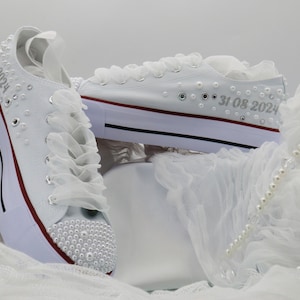 May include: White canvas sneakers with pearl embellishments and a lace trim. The shoes have the date "31.08.2024" written on them.