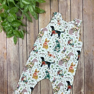 May include: White baby overalls with a floral print featuring silhouettes of dogs. The dogs are outlined in black and filled with floral patterns.