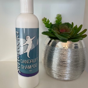 May include: White plastic bottle of dandruff shampoo with a blue and white label. The label features a woman with her arms raised and the text "Dandruff Shampoo 8oz."