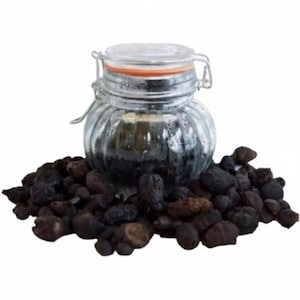 May include: A clear glass jar with a hinged lid, filled with a dark substance, sits on a pile of dark, irregularly shaped objects. The jar has a decorative, ribbed design. The objects appear to be dried, possibly natural, items.