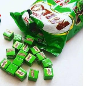 Może przedstawiać: Zielona torba z kostkami energetycznymi Milo, z kilkoma kostkami rozsypanymi. Kostki są pakowane pojedynczo w zielone opakowania z logo Milo i napisem "Energy Cube". Torba jest również zielona z logo Milo.