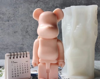 May include: A pink bear-shaped silicone mold and a white silicone mold for making candles. The bear mold has a simple design with no details. The other mold has a textured surface.