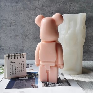 May include: A pink bear-shaped silicone mold for making candles or soap. The mold is next to a finished pink bear-shaped candle.