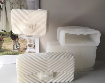 May include: Three white, rectangular, quilted, handbag-shaped candle molds. The molds are made of silicone and have a textured surface.