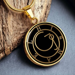 May include: A gold-coloured pendant necklace. The pendant features a black centre with gold lettering spelling out letters around the edge. The circular design includes the letters "H", "I", "S", "M", "A", "E", and "L". The chain is also gold.