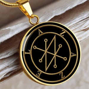 May include: Gold-tone pendant necklace with a circular black pendant. The pendant has gold-coloured symbols and the letters A, Z, and E. The pendant hangs from a gold chain. The design is intricate and detailed.