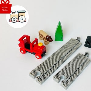 Può includere: Un treno giocattolo rosso con un camino giallo e ruote nere su un binario grigio. C'è un albero verde, una mucca marrone e un semaforo nero e rosso.