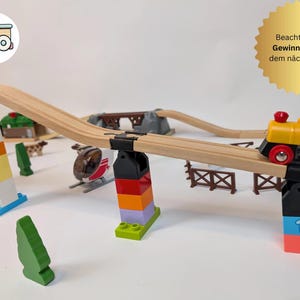 Könnte beinhalten: Ein hölzernes Spielzeug-Zugsset mit einer roten und gelben Lokomotive, einer Holzbrücke und bunten Bausteinen. Der Zug fährt auf einer Schiene, die über die Brücke führt. Es gibt auch ein paar Bäume und anderes Zubehör im Set.