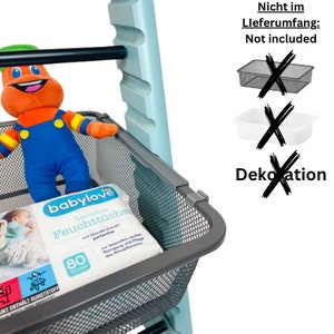 Könnte beinhalten: Ein blaues Metallregal mit einem grauen Drahtkorb. Der Korb enthält eine Packung Babyfeuchttücher und ein Stofftier. Der Text auf der Packung lautet "babylove Sensitive Feuchttücher". Der Text "Nicht im Lieferumfang: Not included" ist in Schwarz auf weißem Hintergrund geschrieben. Ein grauer Drahtkorb, ein weißer Plastikbehälter und ein schwarz-weißes Schild "Dekoration" sind mit einem schwarzen X durchgestrichen.