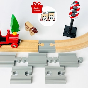 May include: A red toy train engine with a gray and white train car on a wooden train track. The track includes a curved section, a straight section, and a gray plastic switch track. There is a red and white traffic light, a green tree, and a brown cow figurine on the track.