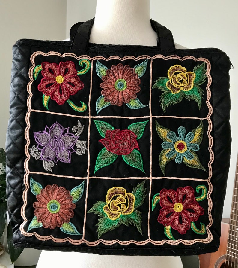 May include: Black quilted tote bag with a zipper closure and two top handles. The bag features a patchwork design with nine embroidered floral motifs in various colors, including red, yellow, green, blue, and purple.