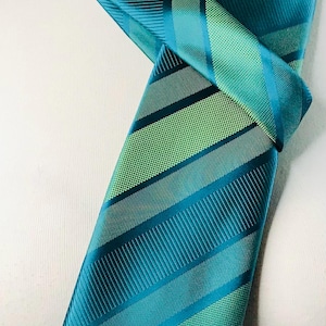 May include: A teal and green striped tie with a diagonal pattern. The tie is tied in a knot and is displayed on a white mannequin.
