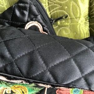 May include: Black quilted pillow with a zipper closure and embroidered floral details in shades of green, yellow, brown, and blue.