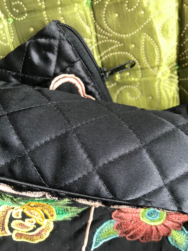 May include: Black quilted pillow with a zipper closure and embroidered floral details in shades of green, yellow, brown, and blue.