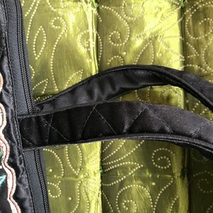 May include: Black quilted tote bag with a zipper closure and two black handles. The bag has embroidered floral details in shades of pink, green, and brown.