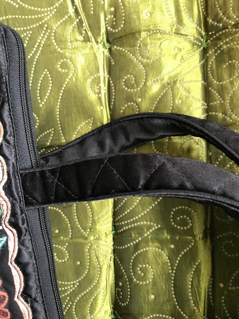 May include: Black quilted tote bag with a zipper closure and two black handles. The bag has embroidered floral details in shades of pink, green, and brown.
