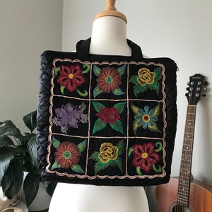May include: Black quilted tote bag with a patchwork design of colorful embroidered flowers. The bag has two top handles.