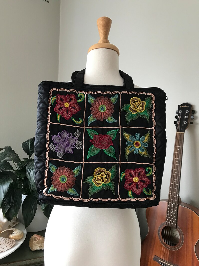 May include: Black quilted tote bag with a patchwork design of colorful embroidered flowers. The bag has two top handles.