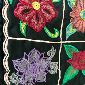May include: A black fabric with embroidered flowers in shades of red, purple, green, and yellow. The flowers are arranged in a grid pattern.