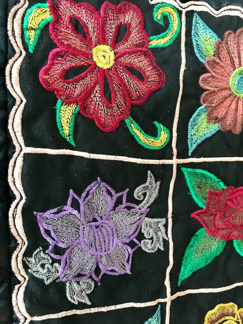 May include: A black fabric with embroidered flowers in shades of red, purple, green, and yellow. The flowers are arranged in a grid pattern.