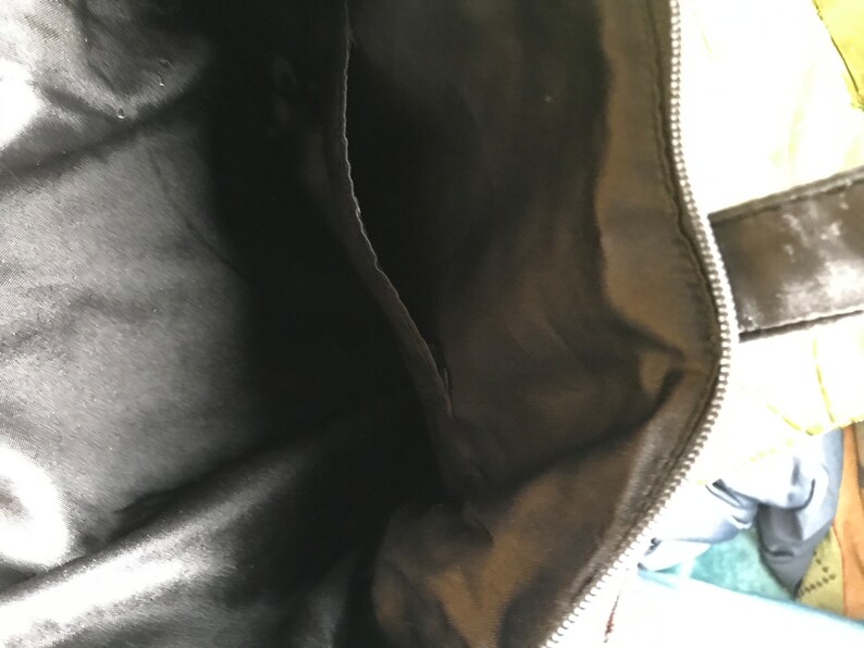 May include: The inside of a black bag with a zipper. The lining is a smooth, black fabric.