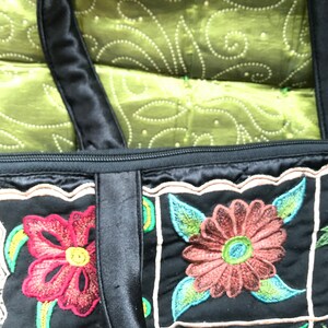 May include: Black quilted tote bag with embroidered floral designs in shades of red, green, and brown. The bag has two black straps and a zipper closure.
