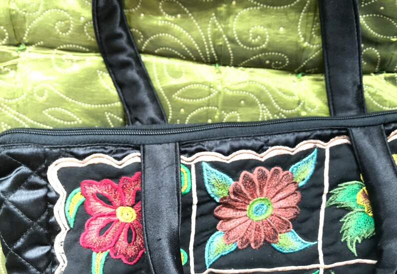 May include: Black quilted tote bag with embroidered floral designs in shades of red, green, and brown. The bag has two black straps and a zipper closure.