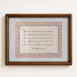 Può includere: Una cornice rettangolare in legno contenente un pezzo di tessuto con il testo May the Lord bless you and keep you. May the Lord make His face shine upon you and be gracious to you. May the Lord turn His face toward you and give you His peace. Numbers 6:24-26.