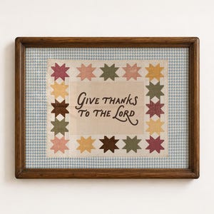 May include: A framed textile wall hanging featuring the text "Give thanks to the Lord" in dark brown script. The central cream-colored fabric is bordered by a pattern of multi-colored eight-pointed stars in shades of pink, yellow, brown, and green.
