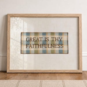 May include: A framed needlepoint art piece featuring a blue, green, and cream plaid background with the dark brown embroidered text "GREAT IS THY FAITHFULNESS" centered within the fabric, enclosed in a light-toned wooden frame with a glass front.