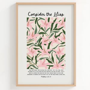 Puede incluir: Una impresión artística enmarcada con un diseño floral de lirios rosas y hojas verdes sobre un fondo crema. El texto "Consider the Lilies" está en la parte superior, con un versículo bíblico debajo. El marco es de color madera clara.