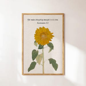 Op de afbeelding: Een ingelijste print met een gele zonnebloem en groene bladeren. De print bevat een citaat uit Prediker 3:11: "Hij maakt alles mooi op zijn tijd."