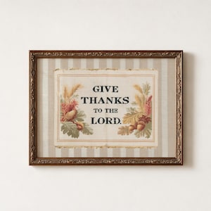 May include: A rectangular framed wall art piece featuring a beige and white striped fabric background. The center displays a cream-colored fabric panel with the black text GIVE THANKS TO THE LORD, flanked by illustrations of wheat and acorns.