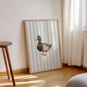 Op de afbeelding: Een ingelijst afdruk van een aquarelillustratie van een eend op een groen-wit gestreepte achtergrond.