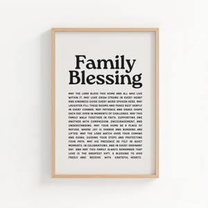 May include: A framed print with the words "Family Blessing" in bold black letters at the top. Below, a lengthy message is printed in a smaller, black, serif font. The frame is a light wood color.