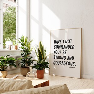 K&ouml;nnte beinhalten: Ein gerahmter Druck mit wei&szlig;em Hintergrund und schwarzem Text, der lautet: "Have I not commanded you? Be strong and courageous. Joshua 1:7"
