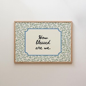Peut inclure: Tableau encadré avec le texte « How blessed are we ». L'œuvre présente un centre crème avec une bordure bleue. Le fond est orné d'un motif de feuilles vertes et de baies bleues, le tout dans un cadre en bois.