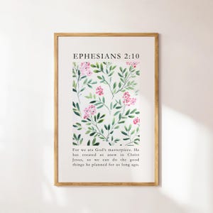 Puede incluir: Un estampado enmarcado con el texto "EPHESIANS 2:10" sobre un diseño floral de flores rosas y hojas verdes sobre un fondo blanco. El marco es de madera marrón claro. El texto de abajo dice: "For we are God's masterpiece..."