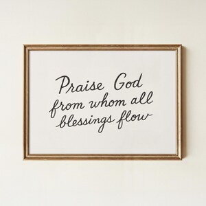 Può includere: Una stampa incorniciata con la scritta "Praise God from whom all blessings flow" in nero. La cornice è dorata e lo sfondo è bianco.