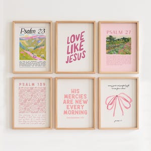 May include: Six framed prints with pink and white designs and text. The prints feature bible verses and inspirational quotes. The prints are arranged in a grid pattern on a white wall.