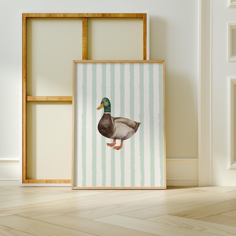 Op de afbeelding: Een ingelijst afdruk van een aquarelillustratie van een wilde eend op een lichtgroene en witte gestreepte achtergrond.