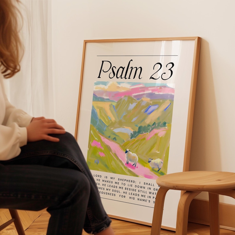 May include: A framed print of Psalm 23 with a colorful landscape painting of rolling hills and a winding path. The painting features two white sheep in the foreground. The text "Psalm 23" is in a large, bold font at the top of the print.