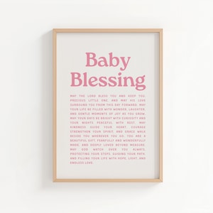 Op de afbeelding: Een ingelijste print met de woorden "Baby Blessing" in roze script. De print bevat een oprechte boodschap in een eenvoudig, elegant lettertype, perfect voor een kinderkamer. De lijst is licht van kleur.