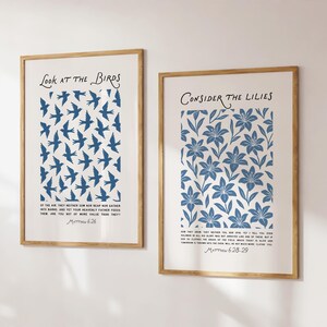 May include: Two framed art prints. The left print says "Look at the Birds" and features blue bird silhouettes. The right print says "Consider the Lilies" and has a blue floral pattern. Both prints have text at the bottom.